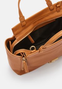 Sac à main en cuir marron avec deux poignées, compartiment zippé ouvert, doublure intérieure noire et détails métalliques dorés.