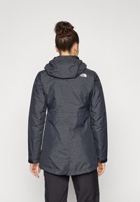 Mörkgrå, vattentålig parka med huva, elastisk midja och logga på övre ryggen, med en strukturerad tyg och långa ärmar.