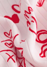 Lyserødt strikket stof med røde kursivskrift og symboler, der skaber et tekstureret, blødt udseende med synlige ribbet detaljer.