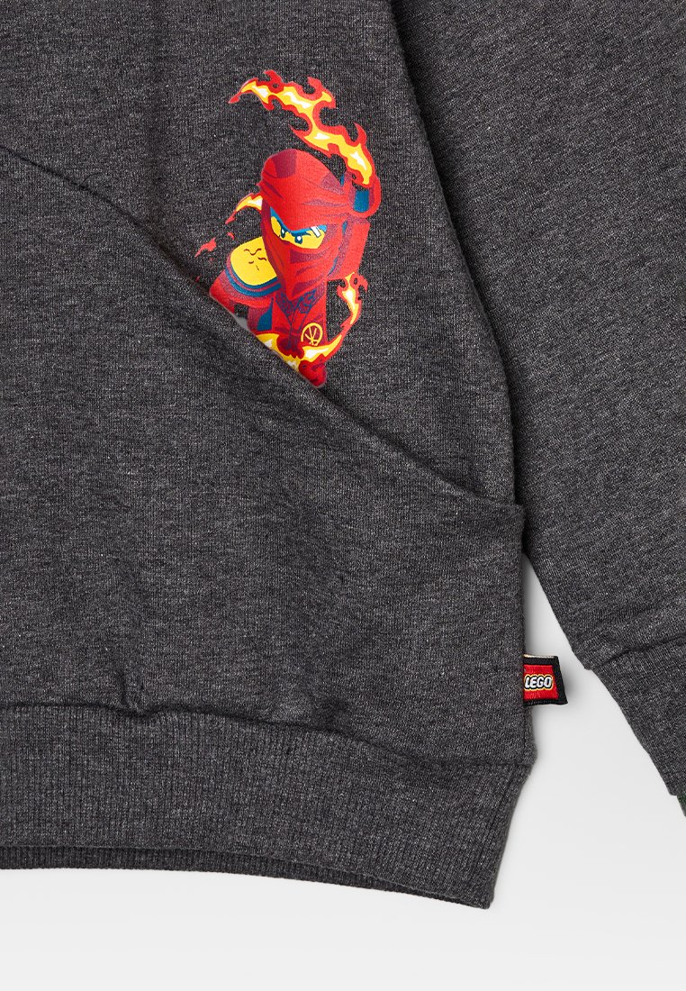 Grauer Hoodie mit strukturierter Oberfläche. Feiert ein lebhaftes Druckdesign eines roten Ninjas mit Flammen. Inklusive eines kleinen LEGO-Logos.