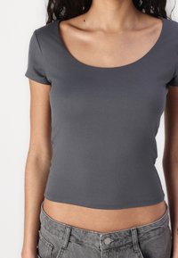 T-shirt gris ajusté avec un col rond et des manches courtes, fabriqué en tissu doux, associé à un short en denim gris taille haute.