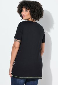 Camiseta de algodón negra con mangas cortas, que presenta un dobladillo curvado y acentos de costura verde. La parte posterior muestra un diseño liso y sencillo.