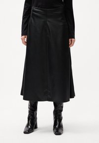 Sort læder maxiskørt med en glat tekstur, høj talje og rene linjer, parret med slanke sorte hæleboots.