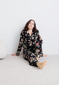 Bloemmotief pyjama's van zwarte stof; bevat een gebuttonde blouse met lange mouwen en bijpassende broek, met een relaxte pasvorm en zachte textuur.