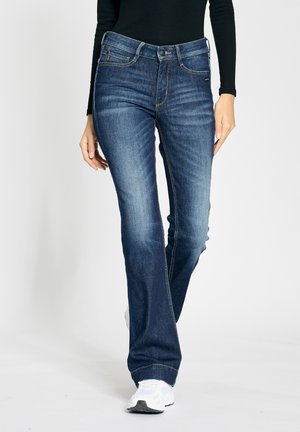 Blue denim jeans with a mid-rise waist, slight whiskering on the thighs, and contrasting stitching. Fitted through the hips, flared at the hem.