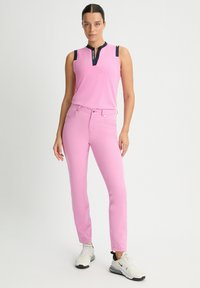 Pink sleeveless top with a navy collar and shoulder accents, paired with pink fitted jeans and white sneakers. Smooth, stretchy fabric.