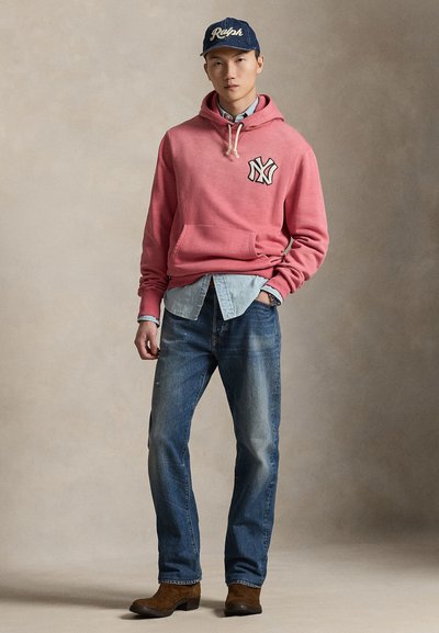 Sudadera con capucha roja con logo, camisa de mezclilla debajo, vaqueros azules y botas marrones. Textura suave, ajuste casual, apariencia en capas con colores contrastantes.