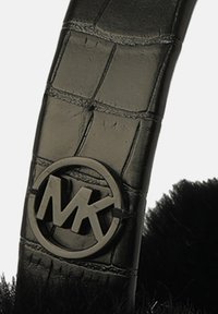 Bracelet en cuir noir avec motif crocodile, comportant un logo MK circulaire et un accent noir duveteux.