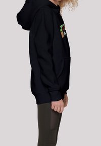 Sudadera negra con un bolsillo frontal, que presenta un texto gráfico colorido en el pecho, combinada con leggings verde olivo. La tela parece suave.