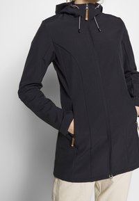 Giubbotto nero con cappuccio, chiusura con zip, due tasche laterali e cordini regolabili. Presenta un tessuto testurizzato e una fodera morbida.