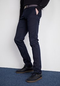 Tmavě modré slim-fit kalhoty vyrobené z bavlněné směsi, se bočními kapsami a texturovaným šedým opaskem. V kombinaci s černými sportovními botami.