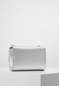 Clutch bag metallica argento con superficie testurizzata, forma rettangolare e una leggera lucentezza. Presenta una chiusura con zip e una tracolla a catena removibile.