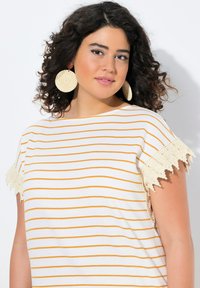 Pruhovaný top s krátkými rukávy v bílé a žluté barvě s krajkovým lemem na rukávech. Kulatý výstřih a měkká textura, doplněno velkými kulatými náušnicemi.