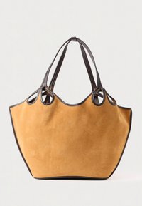 Semišová taška typu tote v barvě hořčice s tmavě hnědým koženým lemem a rukojetí. Měkká textura, prostorná a úhlový design s zaoblenými vrcholy.