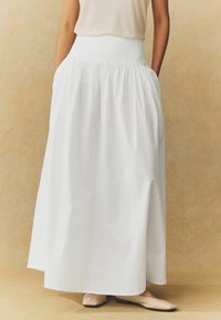 Jupe longue blanche en tissu léger, dotée d'une taille haute et de plis froncés. Texture douce avec un design fluide.