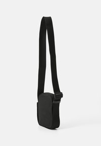 Borsa a tracolla nera con una texture morbida, forma rettangolare, tracolla regolabile e chiusura con zip. Design minimalista, senza ulteriori motivi.