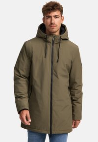Parka waterproof vert olive avec capuche, fermeture éclair à l'avant, cordon de serrage et poches latérales. Texture lisse avec un design moderne et épuré.