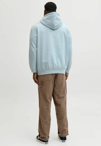 Sweat à capuche bleu clair avec poignets et ourlet côtelés, associé à un pantalon cargo beige avec poches latérales et coupe ample. Baskets noires.