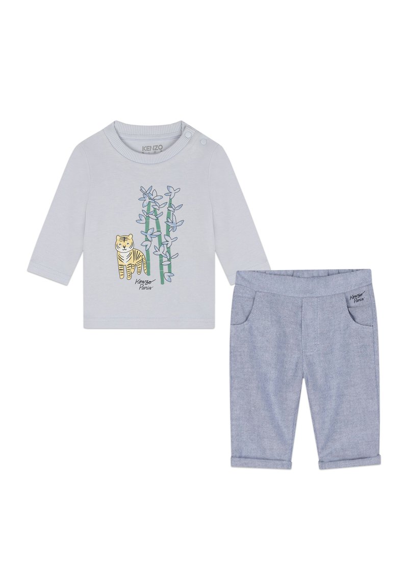 Chemise à manches longues gris clair avec un graphique de tigre et un motif de bambou ; associée à un pantalon bleu à ourlet roulé avec poches latérales.