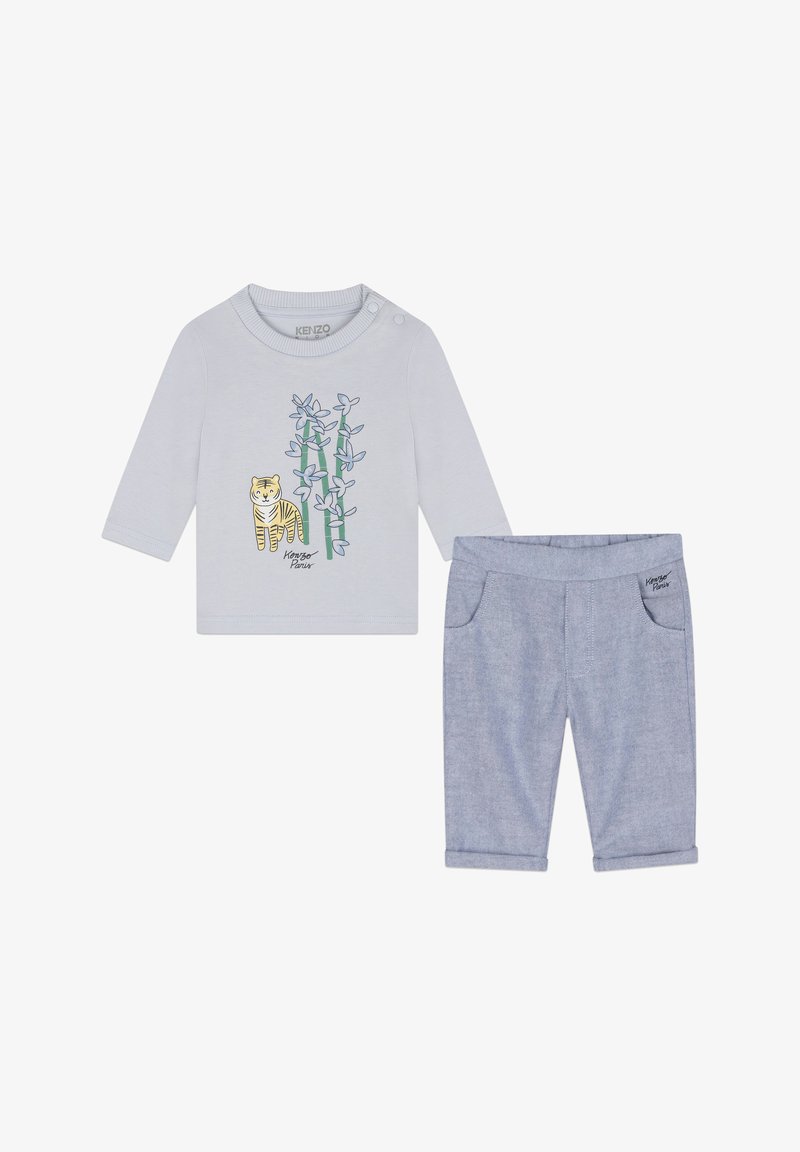 Chemise à manches longues gris clair avec un graphique de tigre et un motif de bambou ; associée à un pantalon bleu à ourlet roulé avec poches latérales.