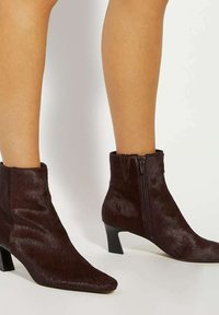 Brown faux fur ankle boots with a pointed toe and zip closure, featuring a low kitten heel and smooth texture.