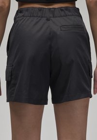 Pantaloni cargo neri con vita elastica, tasche laterali e una tasca posteriore. Realizzati in tessuto leggero con una consistenza liscia.