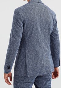 Blazer med fiskbensmönster i blå och vita nyanser, med skräddarsydd passform, strukturerade axlar och tvåknappsstängning med kontrasterande tygdetaljer.