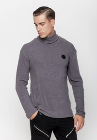 Szary prążkowany sweter z golfem, z długimi rękawami, z okrągłym czarnym logo na klatce piersiowej i fakturowanym wzorem tkaniny.