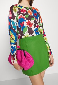 Maglione a maglia floreale con fiori multicolori su sfondo marrone scuro, abbinato a una mini gonna verde brillante e una borsa intrecciata rosa.