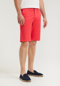 Röda bomullsshorts med knappstängning fram, sidofickor och rak skärning, ihop med marinblå slip-on espadriller.