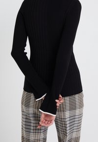 Zwarte geribbelde langslijf top met een slim-fit ontwerp. De zoom heeft witte accenten. Gepaard met geruite beige en zwarte broek.