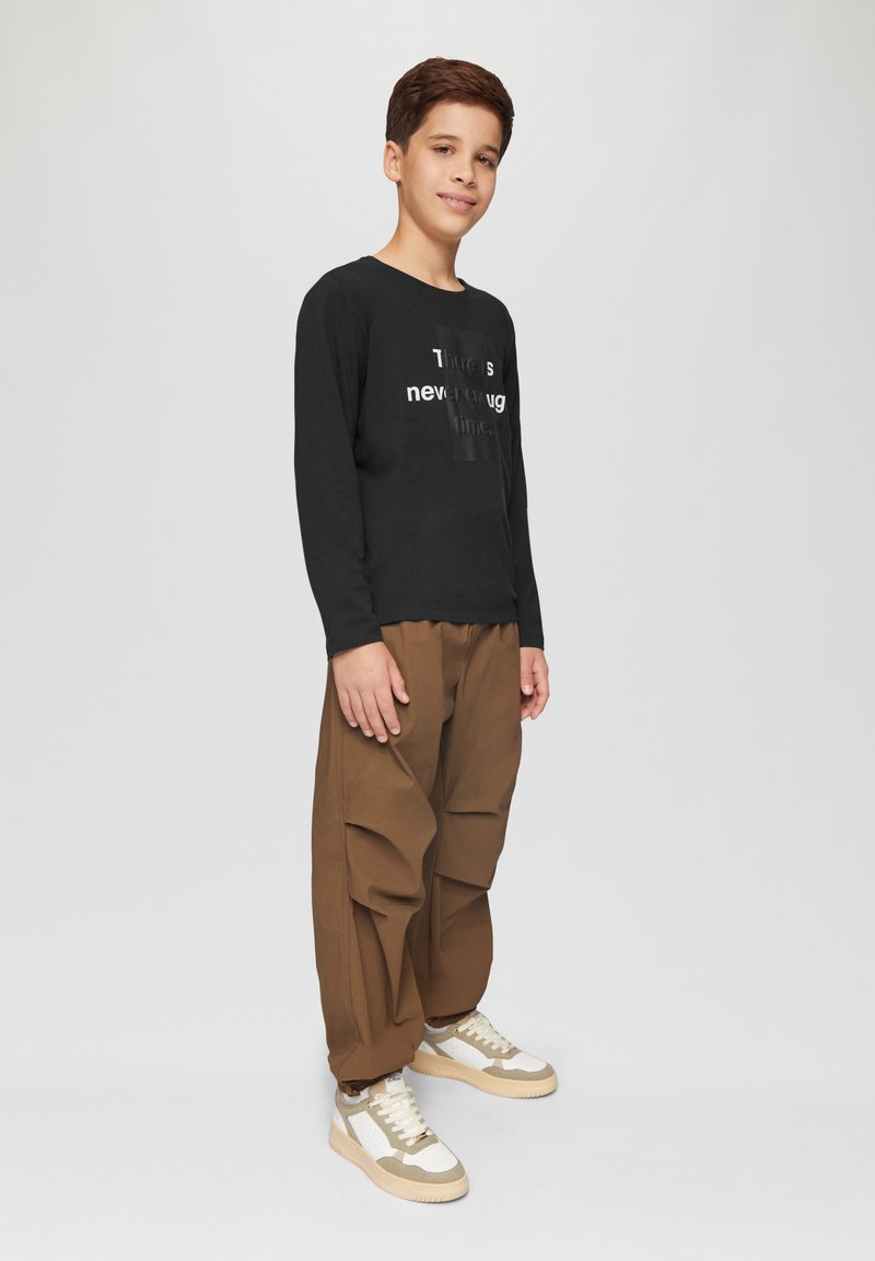 Zwarte longsleeve shirt met witte tekst, bruine baggybroek en beige sneakers met witte accenten. Relaxte pasvorm, zachte stof.