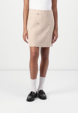 Jupe mini en tweed beige avec deux accents de boutons métalliques, présentant un tissu texturé, une silhouette droite et une longueur au-dessus de mi-cuisse.