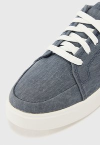 Sneaker de lona azul com atacadores brancos, bico redondo e parte superior texturizada. Apresenta uma sola de borracha branca em contraste e detalhes de costura.