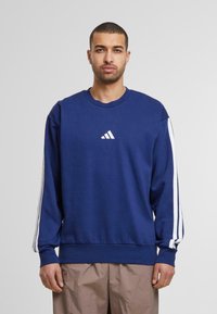 Jūrinis džemperis su baltu Adidas logotipu krūtinėje, turi baltas šonines juosteles. Apvalaus kaklo dizainas ir suglebę elastiniai rankogaliai bei juostos. Minkšta medžiagos tekstūra.
