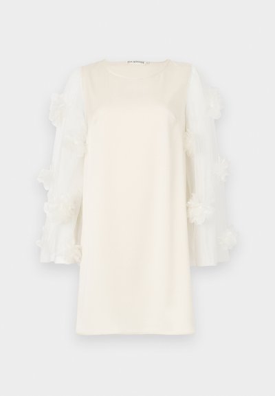 Balta kleita ar gludu audumu, puskcaurspīdīgām piedurknēm, kas izrotātas ar kārtām ziedu aplikācijām. Apaļa izgriezuma, virs ceļgaliem.