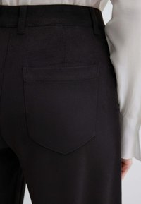 Schwarze Wildledenhose mit einer Gesäßtasche, die über eine glatte Textur und einen geraden Schnitt verfügt. Mit Gürtelschlaufen an der Taille.