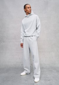 Sudadera de gran tamaño en gris claro y pantalones de chándal holgados a juego, fabricados en un tejido suave. El conjunto presenta una capucha y bolsillos laterales. Zapatillas blancas incluidas.