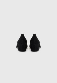 Scarpe block-heeled in suede nero con punta affusolata. La vista posteriore mostra una texture liscia e un tacco robusto, design minimale senza decorazioni.