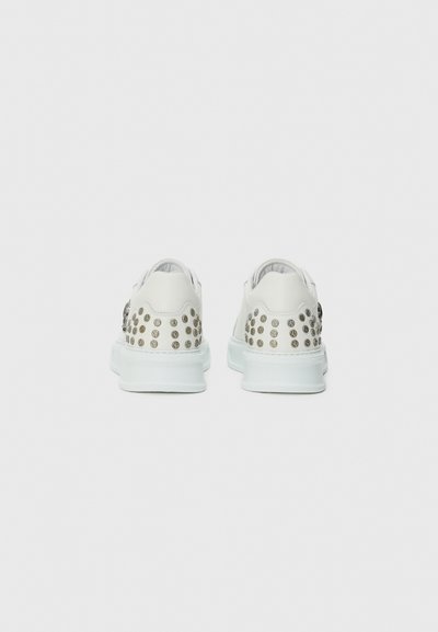 White leather sneakers featuring studded accents on the heel, a smooth upper, and a solid rubber sole in a light color. Flat laces included.