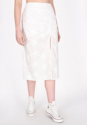 Witte rok tot op de knie met bloemtextuur en een zijspleet, gedragen met witte hoge sneakers. Lichtgewicht stof, strakke tailleontwerp.