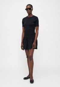 Zwarte aansluitende top met korte mouwen, gecombineerd met een zwarte rok met een smocked taille en textuurstof. Zwarte ballerina's maken de look compleet.