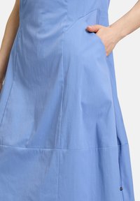 Helles blaues Kleid aus glattem Stoff, mit einer Seitentasche, Nahtdetails und einer entspannten Silhouette mit geflammtem Saum.