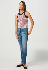 Top de tirantes a rayas rojas y blancas con ribete azul marino, combinado con jeans azules de corte ajustado y zapatos planos negros. El top tiene un escote redondeado.