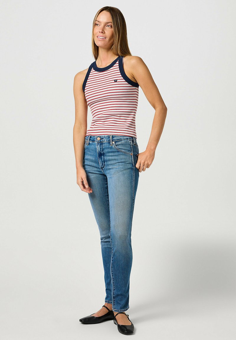 Top a righe rosse e bianche con bordi blu navy, abbinato a jeans slim fit blu e ballerine nere. Il top presenta un collo rotondo.