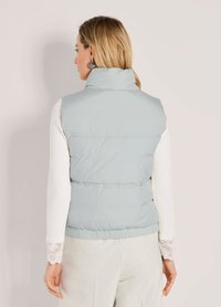 Hellblaues Puffer-Gilet mit hohem Kragen, darunter gerippte weiße lange Ärmel und ein strukturiertem Saum. Keine auffälligen Beschläge oder Muster sichtbar.