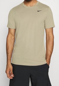 Camiseta de algodón beige con cuello redondo, mangas cortas y un logotipo negro de Nike en el lado izquierdo del pecho. Diseñada para uso casual.