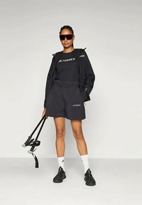 Μαύρο σετ αθλητικών ρούχων που περιλαμβάνει ζακέτα με φερμουάρ, μπλούζα και σορτσάκι, όλα με σήμανση TERREX. Τα αξεσουάρ περιλαμβάνουν μαύρα γυαλιά ηλίου και παπούτσια.