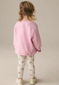 Lyserød sweatshirt med en afslappet pasform, parret med cremefarvede leggings med blomsterprint og små prikker. Neutrale sneakers supplerer outfittet.