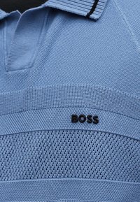 Ανοιχτό γαλάζιο πλεκτό πόλο με υφή και μαύρο λογότυπο "BOSS" στο στήθος κάτω από το γιακά.